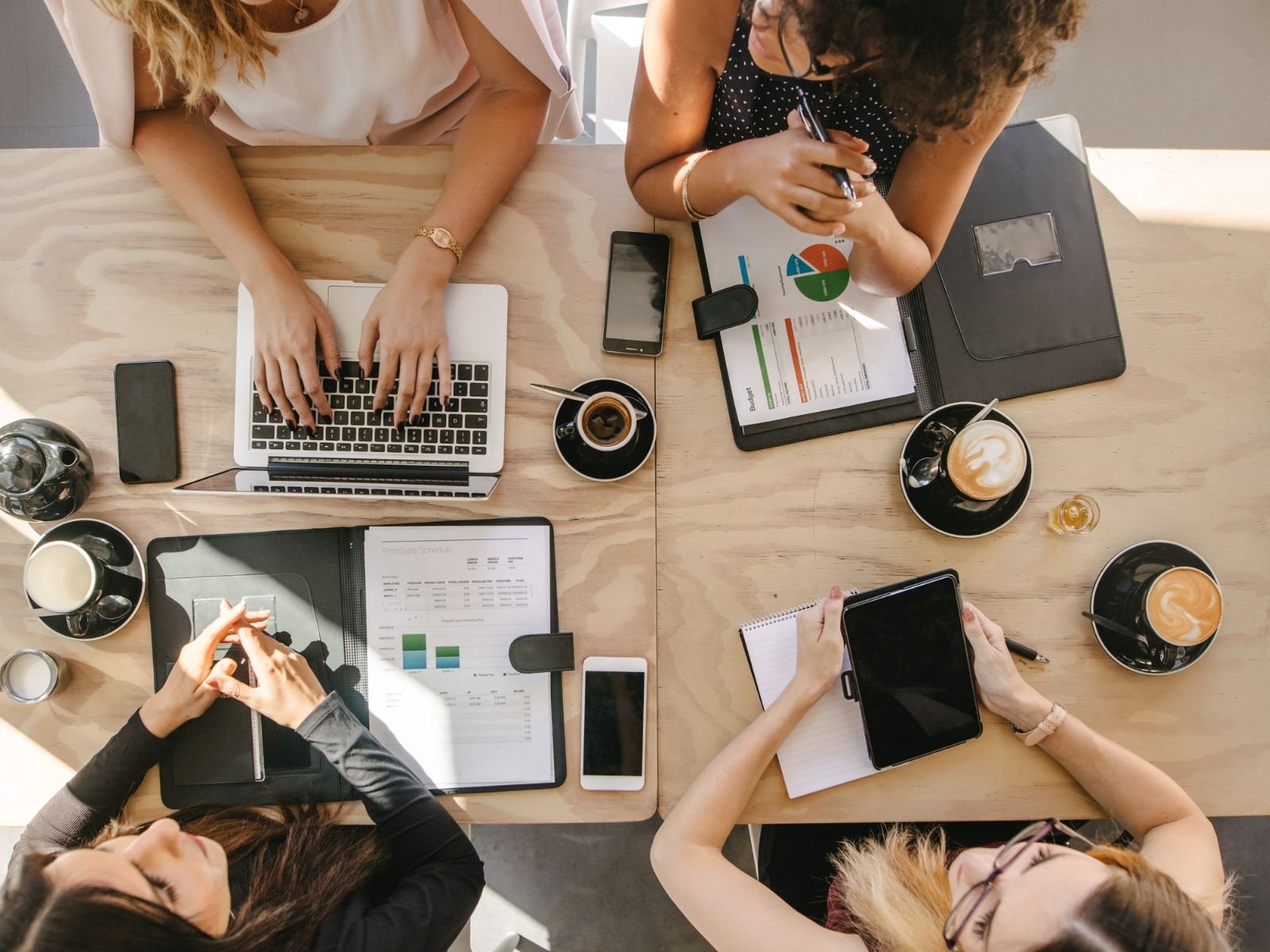 Four women working together around a table with notebooks and coffee